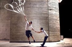 two men are playing with balloons in front of a brick wall and stone building at night