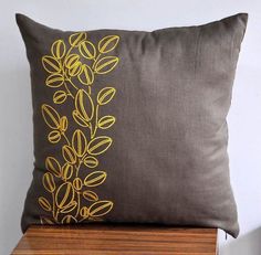 a brown pillow with yellow leaves on it sitting on top of a wooden shelf next to a white wall