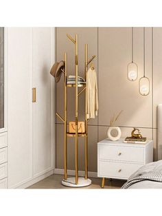 a gold coat rack with clothes hanging on it in a bedroom next to a white dresser