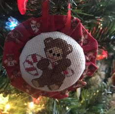 a cross stitch ornament hanging from a christmas tree with red ribbon and teddy bear on it