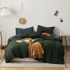 a bed with green sheets and blankets in a white room next to a wooden floor