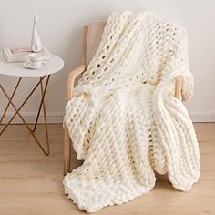 a white knitted blanket sitting on top of a wooden chair next to a table