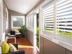 a living room filled with furniture and windows covered in white shutters, next to a wooden floor