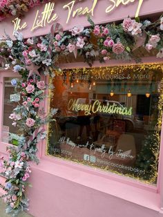 a pink store front decorated with flowers and greenery