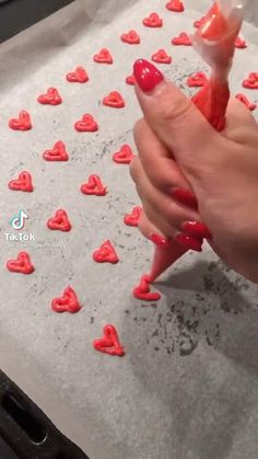 a person is making hearts out of candy on a sheet of baking paper with red icing