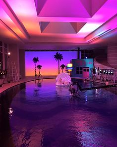 an indoor swimming pool with purple lighting and palm trees