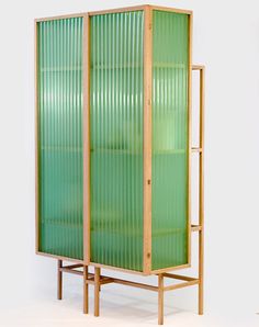 a tall green cabinet sitting on top of a wooden stand next to a white wall