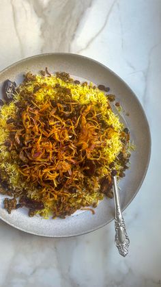 a white plate topped with yellow rice and other food on top of a marble table