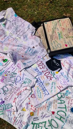 a blanket with writing on it laying in the grass next to an open book and notebook