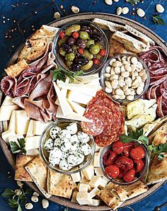 a platter filled with meats, cheeses and other foods on a blue surface