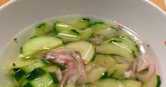 a white bowl filled with cucumbers and onions on top of a wooden table