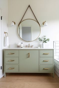 Sleek modern bathroom vanity in soft Evergreen Fog with brass hardware, white quartz countertop, and large round mirror. Large Oval Mirror, Round Mirror Decor, Spa Inspired Bathroom, How To Roll Towels