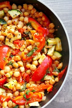 a pan filled with chickpeas, tomatoes and zucchini on top of a wooden table