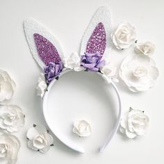 a white headband with purple glitter bunny ears and flowers around it on a white surface