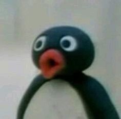 a close up of a toy penguin with its mouth open and eyes wide open, standing in front of a white wall