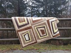 a quilt hanging on a wooden fence in front of some trees and grass with the background of a wooded area