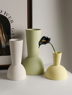 three vases are sitting on a table next to a framed photograph and an art print