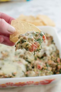 a hand holding a tortilla chip over a bowl of dip