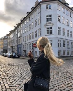 a woman standing on a cobblestone street holding a cell phone up to her ear