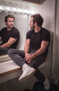 two men sitting on a counter in front of a mirror