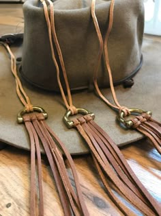 two brown leather tassels are on top of a gray hat with brass hardware