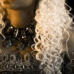 a close up of a mannequin head with curly hair and jewelry on it