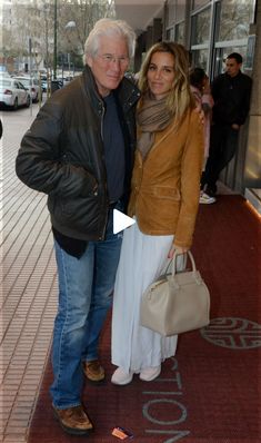 a man and woman standing next to each other in front of a building with people walking by