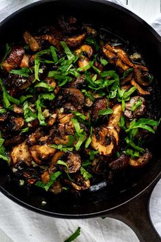 a skillet filled with mushrooms and spinach on top of a white table cloth