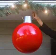 a woman is holding up a giant red christmas ornament