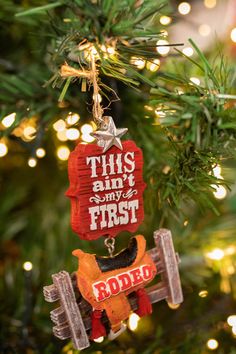 this isn't my first rodeo ornament hanging from a christmas tree with lights in the background