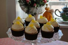 cupcakes with white frosting and yellow decorations on a glass plate in front of a window