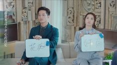 two people sitting on a couch holding up signs in front of them with chinese writing