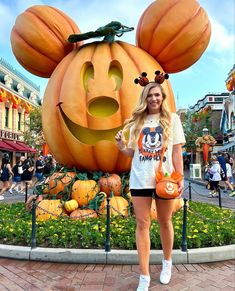 a woman standing in front of a mickey mouse pumpkin