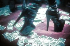 a pair of high heeled shoes sitting on top of a wooden floor covered in money