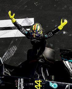 a man with his arms in the air sitting on top of a race car at a track