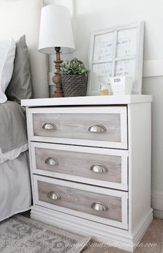 a white dresser with drawers and a lamp on top in a bedroom next to a bed