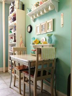 a dining room table with two chairs next to it and shelves on the wall above