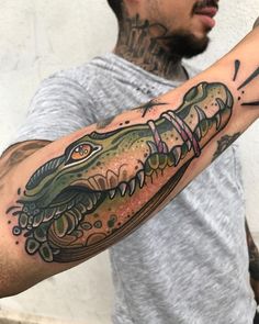 a man with a tattoo on his arm has a large alligator tattooed on it's arm