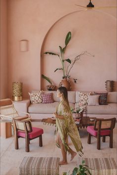 a woman walking through a living room with pink walls