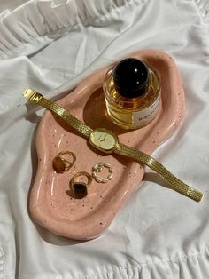 a bottle of perfume sitting on top of a pink tray next to gold rings and earrings