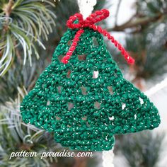 a crocheted christmas tree ornament hanging from a pine tree with red ribbon