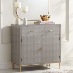 a gray cabinet with gold handles and two candles on top, next to a mirror