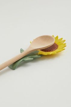 a wooden spoon sitting on top of a yellow sunflower flower with green stems and leaves