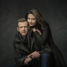 a man and woman are posing for a portrait in front of a dark background,