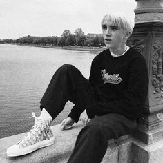 a young man sitting on the edge of a bridge next to a body of water