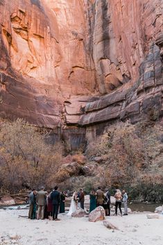 a group of people standing next to each other in front of a mountain side cliff