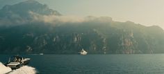 a boat is traveling on the water near mountains and clouds in the sky, with another boat behind it