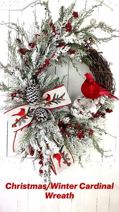 a christmas wreath with red birds and pine cones is hung on a white wooden wall