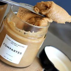 a jar filled with peanut butter on top of a wooden table next to a spoon