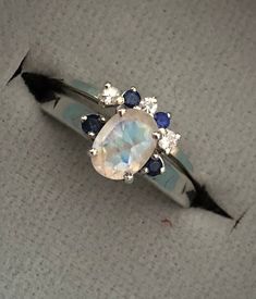 "A unique oval-shaped faceted rainbow moonstone engagement ring set accented with 2 petite genuine blue sapphires complemented with a matching contour wedding band featuring genuine blue and white sapphires handcrafted in sterling silver. Wrapped in a box ready for gift-giving.(r-egt-9) Instagram Video --------------- https://instagram.com/p/Bl3qWYXFgUA/ Can be custom made in any material and gemstones Center stone measure 7mm x 6mm Side Stone measures 2.2mm ----> Please note there is an addi Oval Sapphire Multi-stone Gemstones, White Oval Sapphire Ring, Elegant Sapphire Moonstone Ring In Oval Shape, Diamond Moonstone Ring With Gemstone Accents For Promise, Sapphire Multi-stone Gemstones For Wedding, Diamond-accented Moonstone Ring For Promise, Elegant Sapphire Color Moonstone Ring, Celestial Opal Birthstone Ring In Oval Shape, Celestial Oval Opal Birthstone Ring